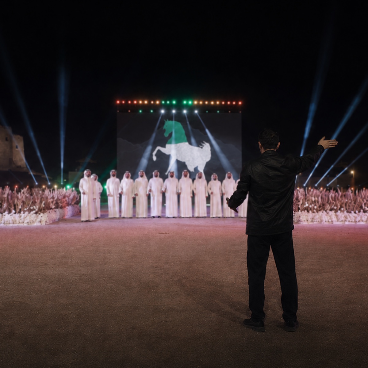 A director in black directing a line of performers in white robes in front of a large screen showing a horse.