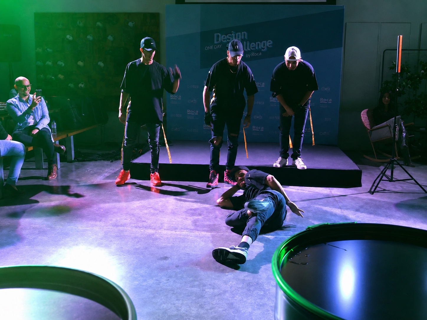 Dancers on a low stage watching a performer spinning on the floor in front of them.