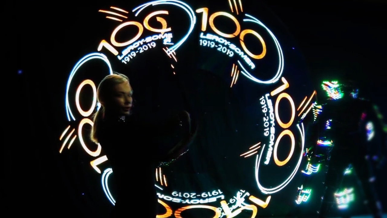 Rings of light-writing reading 100 and 1919-2019 circling a performer in the dark.
