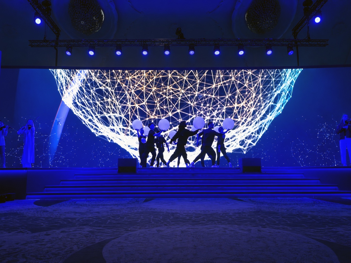 Dancers silhouetted in front of a large screen showing a globe drawn as a network of connected points.