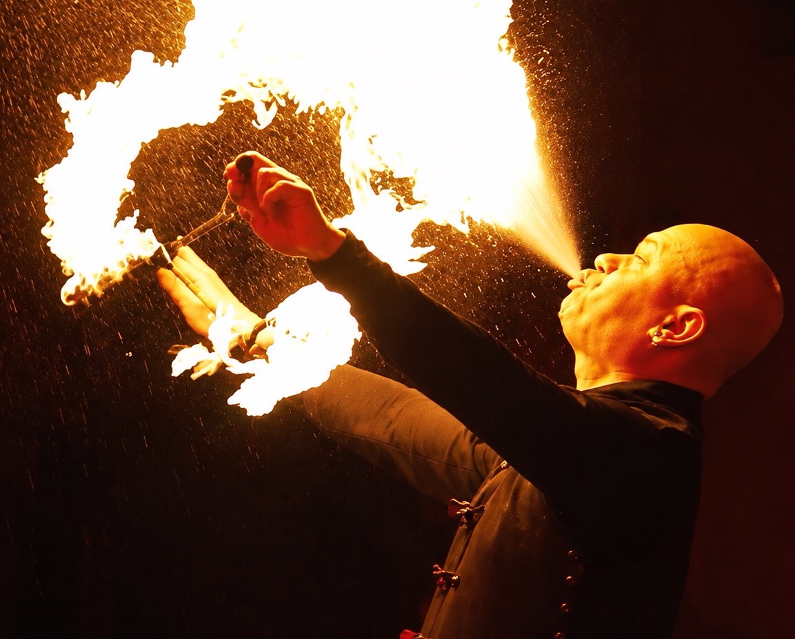 A fire performer breathing a wide plume of flame into the night air.