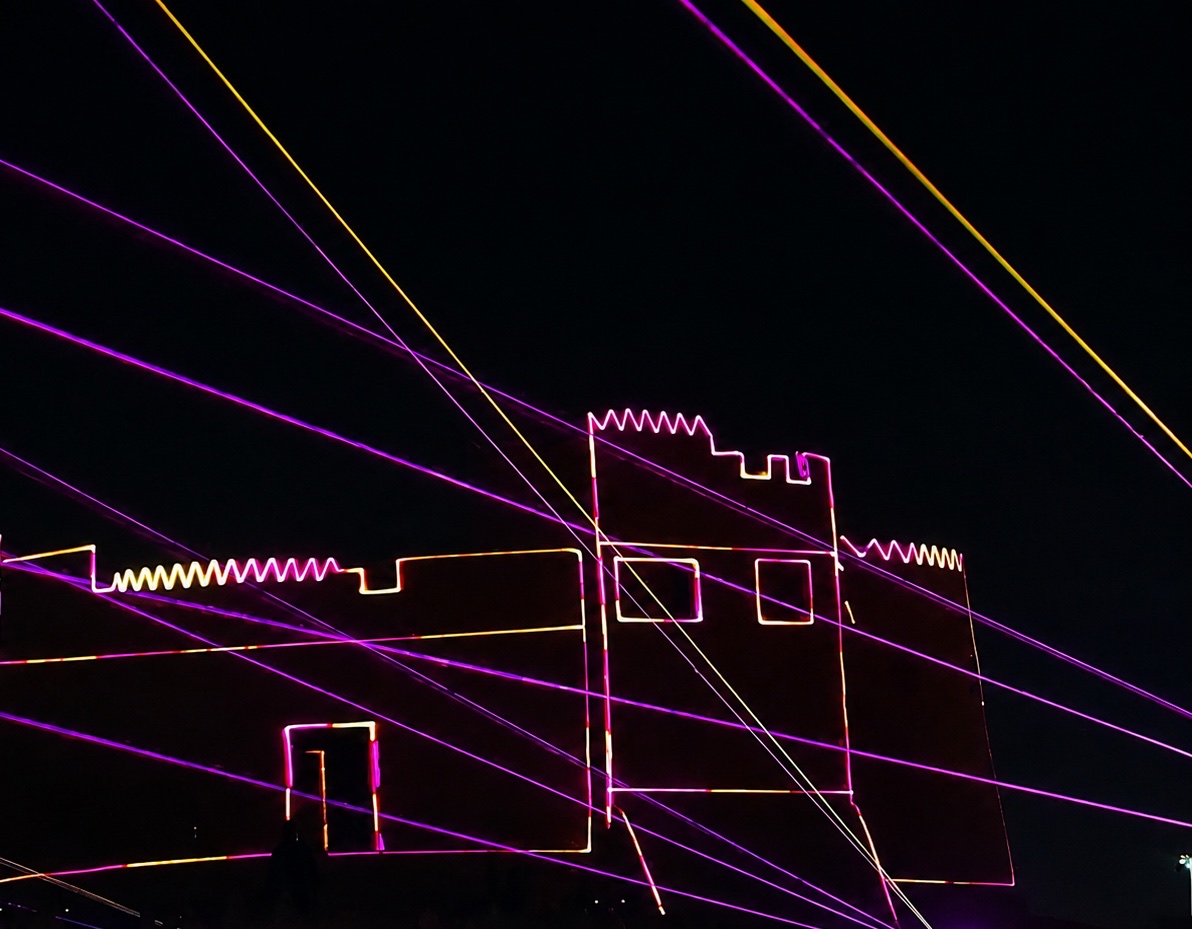 Laser beams crossing above the illuminated outline of a fort drawn in light.