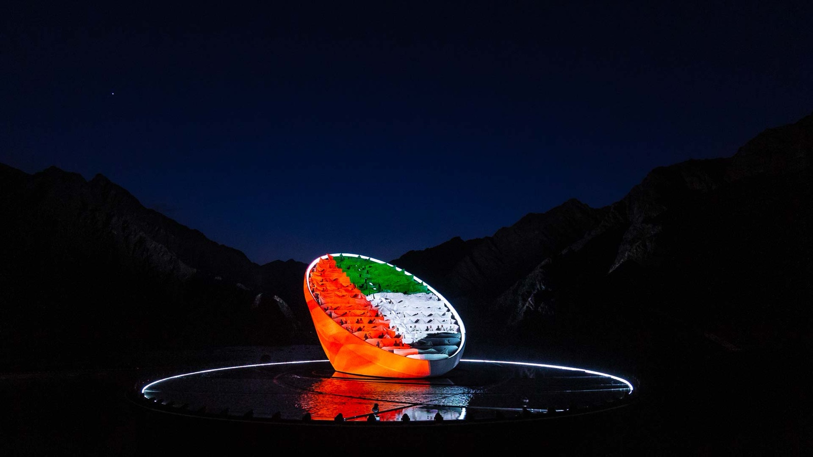 The same sculpture lit in the red, green, white and black of the UAE flag against a night sky.