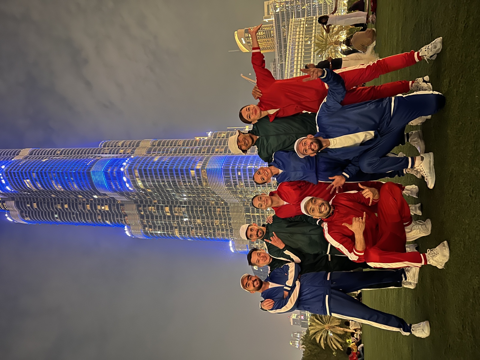 The cast posed together on grass in front of the Burj Khalifa lit blue.