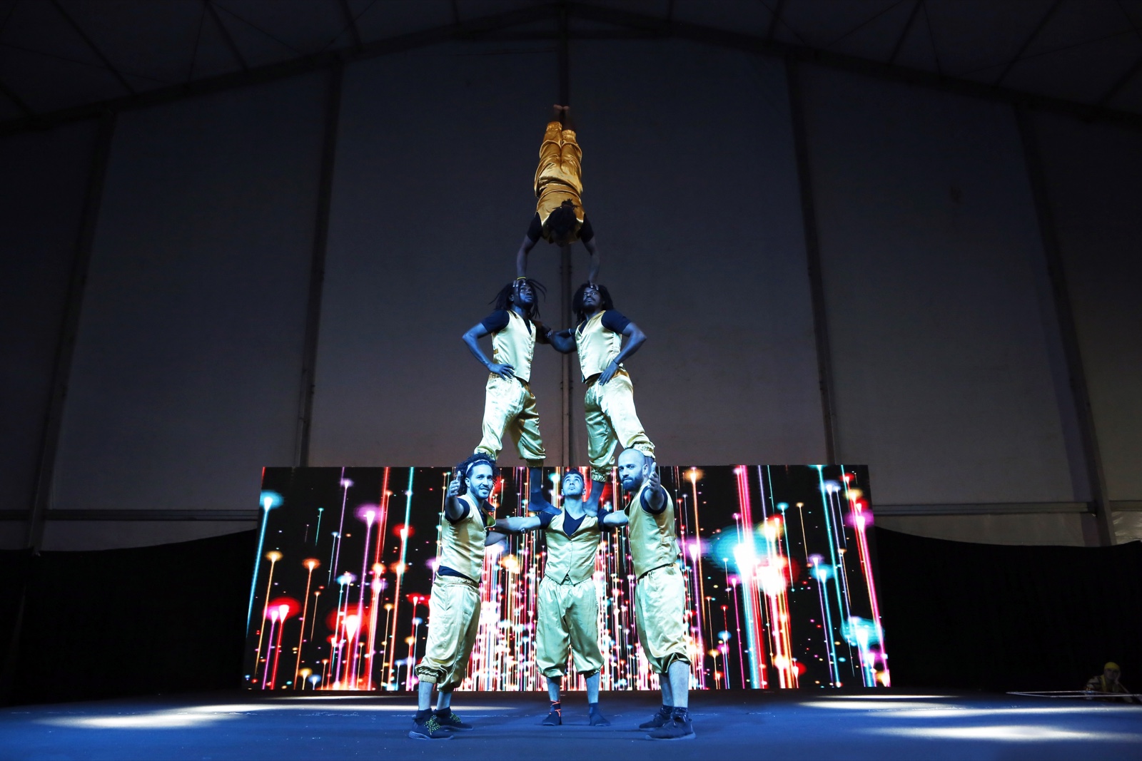 A four-person human pyramid, the performer at the top holding a golden trophy aloft.