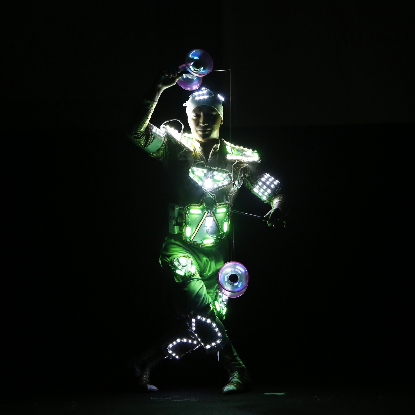 A performer in a green LED costume spinning illuminated diabolos in a darkened tent.