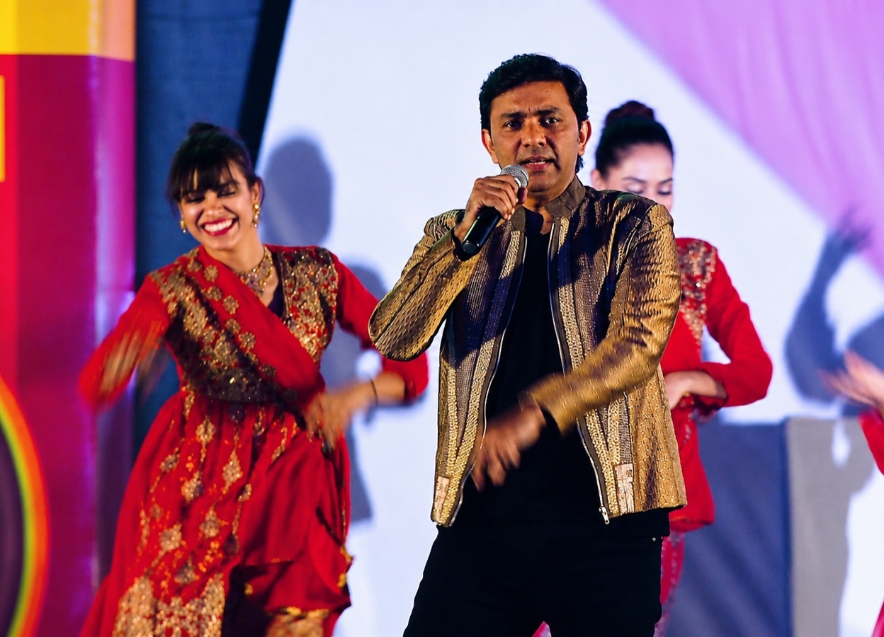 A singer with a microphone downstage while dancers in red move behind.