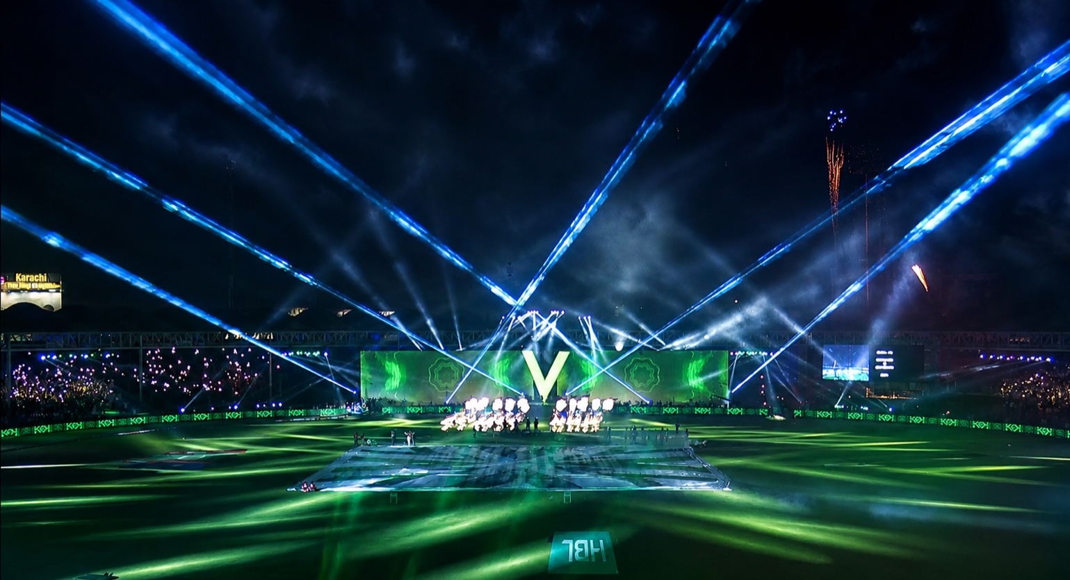 Wide stadium view with green and blue beams converging above the stage.