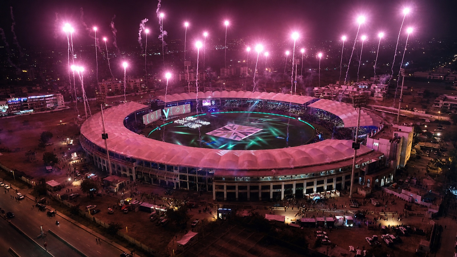 Aerial view of the floodlit stadium with fireworks firing from the roofline.