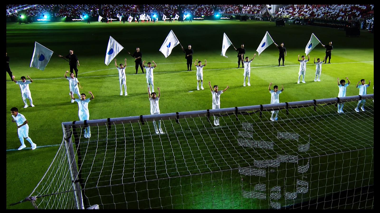 Rows of performers in white holding flags in formation across the pitch.