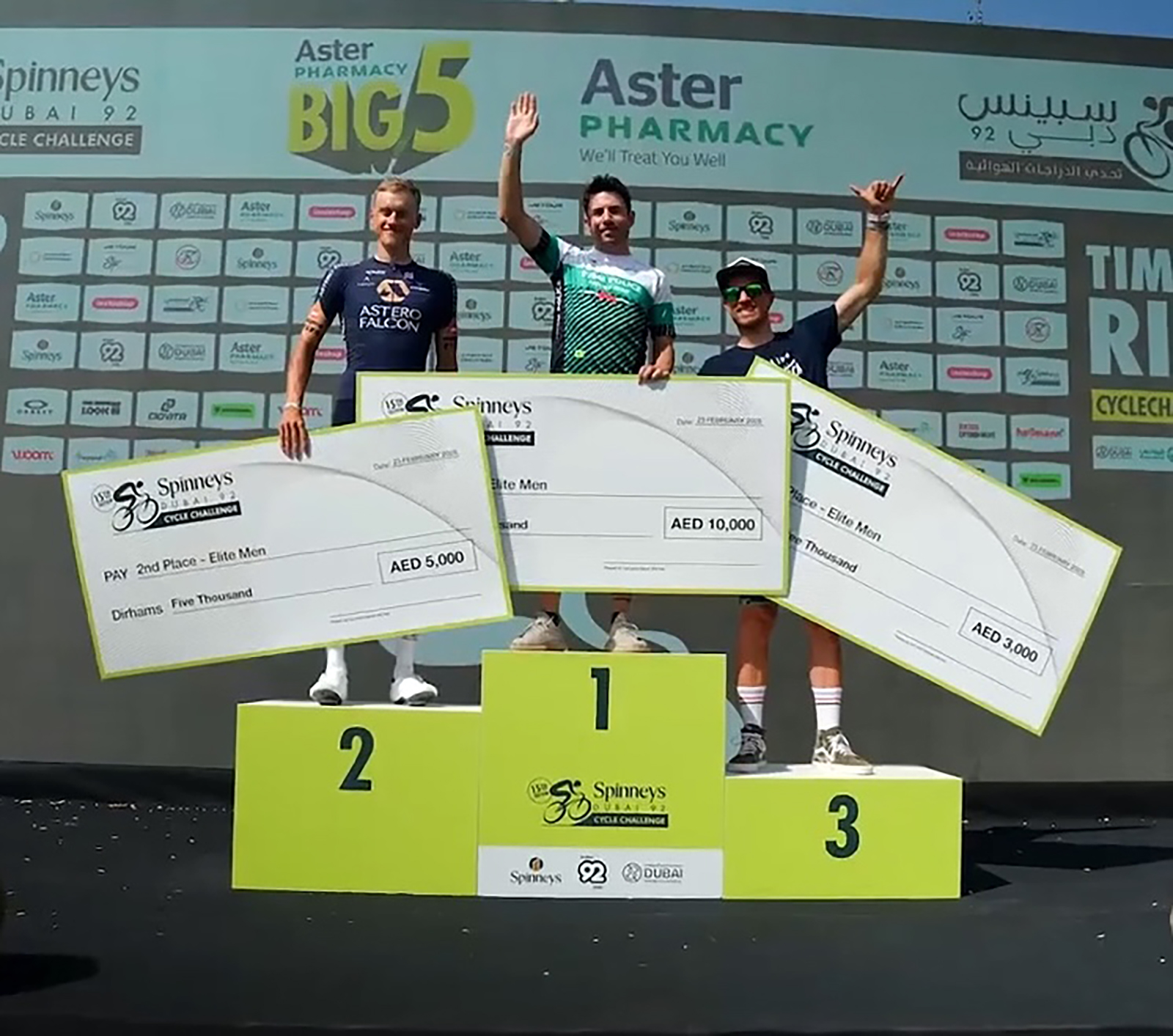 Three cyclists on a winners' podium holding oversized prize cheques.
