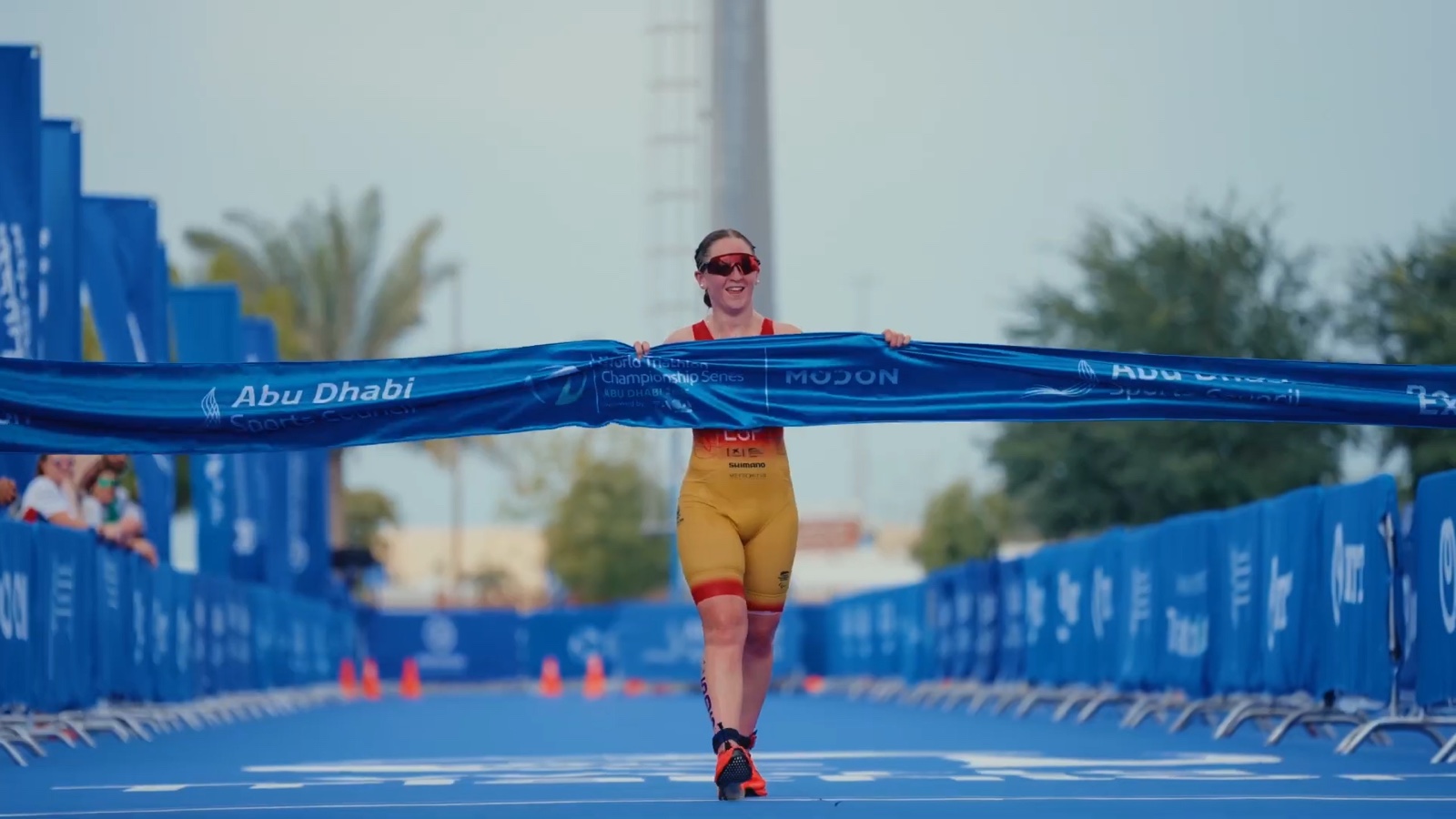 An athlete crossing the finish line and breaking the tape on the blue race carpet.