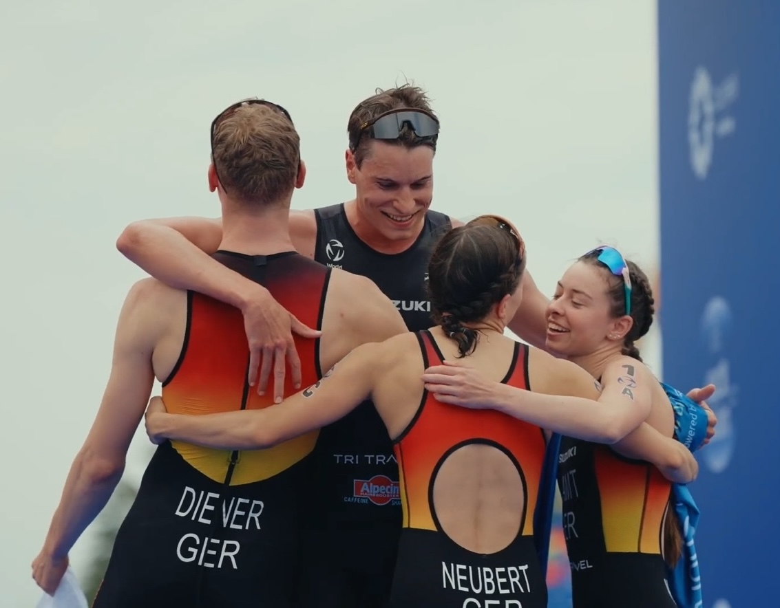 Four athletes in team kit gathered in an embrace in the finish area.